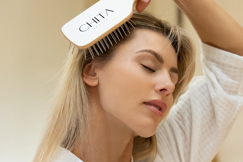 Woman using a hairbrush with 'CHI' branding in a bathroom setting